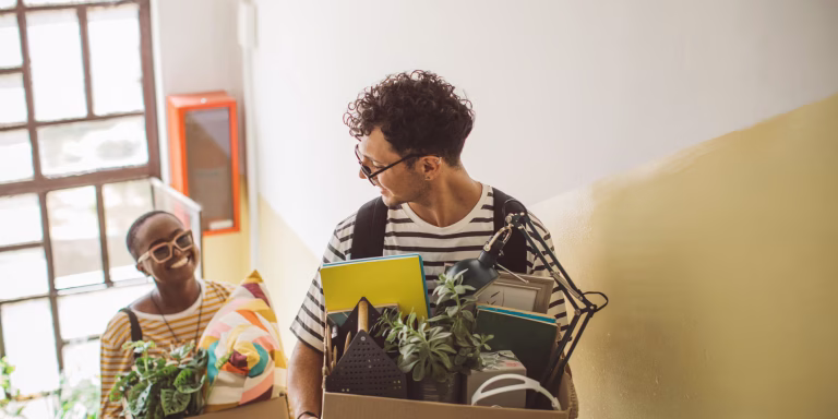 Moving into a college apartment carrying boxes up stairs in new home.